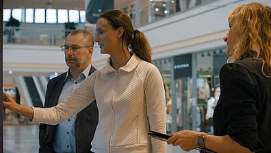 Es sind zwei Frauen und ein Mann zu sehen. Sie betrachten gemeinsam etwas und sprechen darüber.