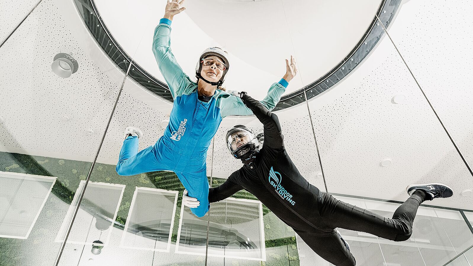 Zwei Personen in Anzügen schweben in einem Windkanal.