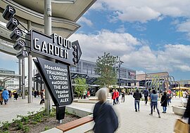 Auf dem Bild ist ein Totempfahl mit der Aufschrift "Food Garden" zu sehen, dahinter stehen Gebäude.