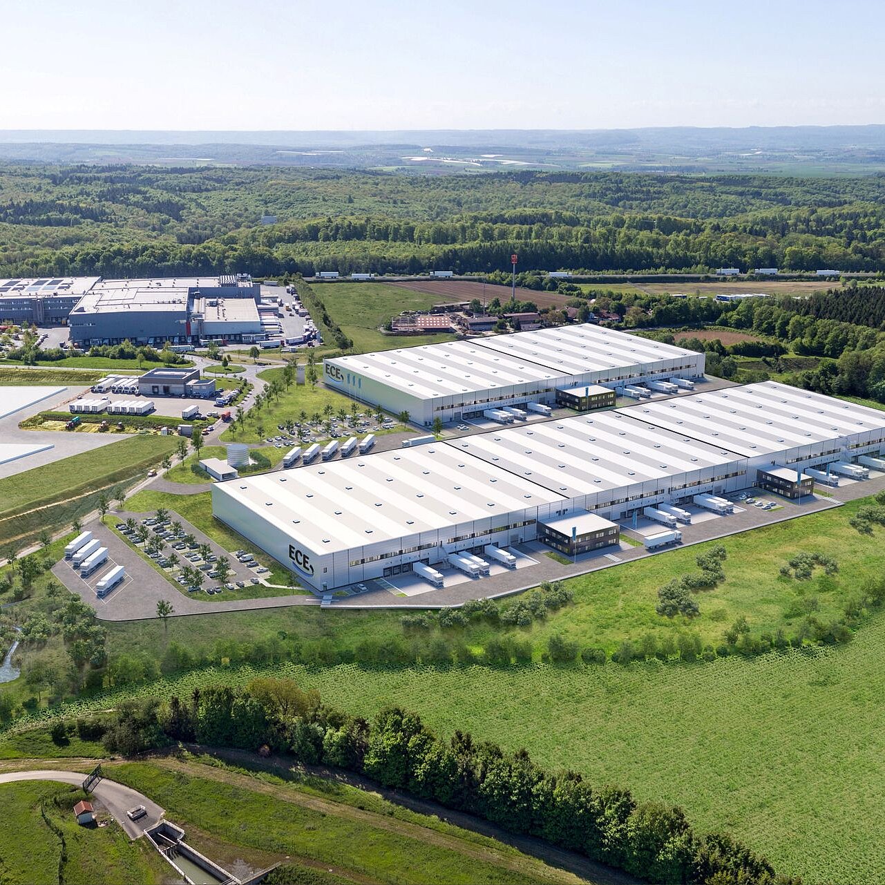 Vogelperspektive auf eine weite grüne Wiese und mittendrin ein großes Logistikgebäude.