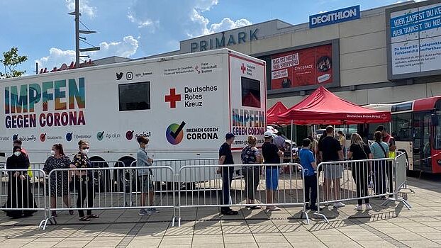 Menschen stehen vor einem Bus mit der Aufschrift &#039;Impfen gegen Corona&#039;.