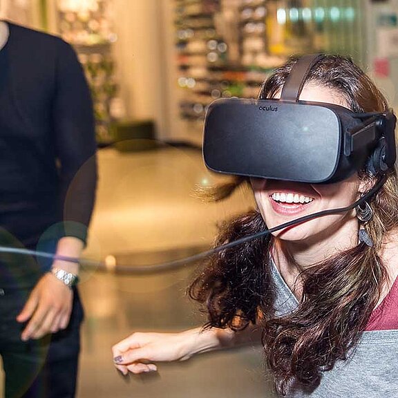 Eine Frau trägt eine schwarze Simulationsbrille und lacht dabei