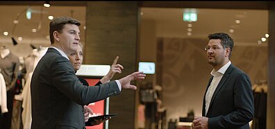 Three people in work clothes stand in front of a display window and exchange ideas
