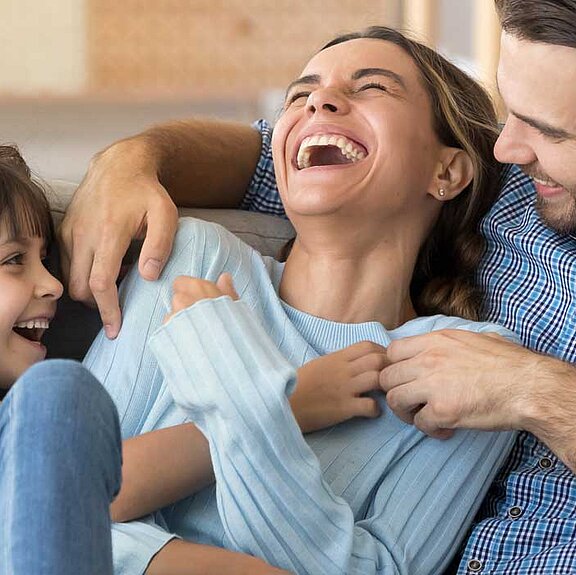 A small family sits on a sofa laughing.