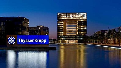 Blick auf ein beleuchtetes ThyssenKrupp-Bürogebäude bei Abend.