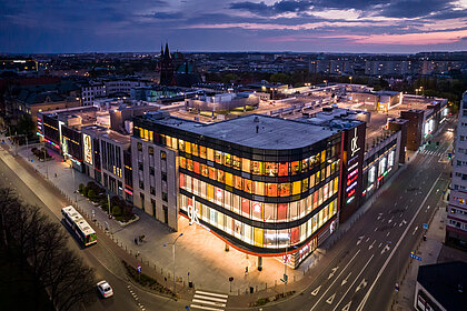 Vogelperspektive auf das beleuchtete Einkaufszentrum Galeria Kaskada am Abend.