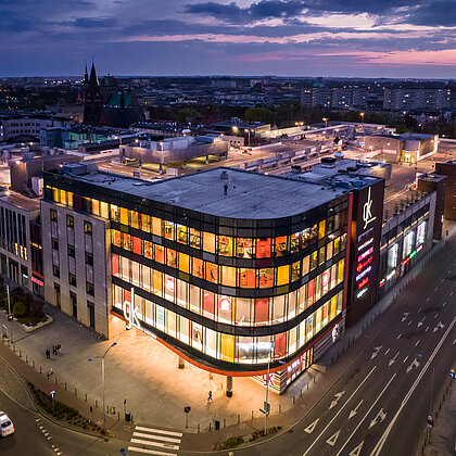 Vogelperspektive auf das beleuchtete Einkaufszentrum Galeria Kaskada am Abend.