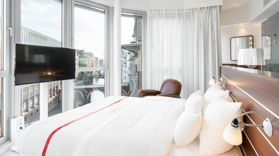 View of a sleeping area in a hotel room with large windows flooded with light.