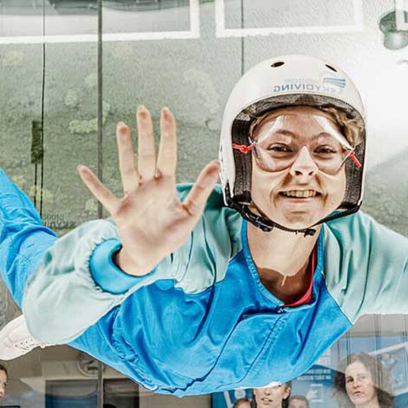 Auf dem Bild ist eine Frau in einem blauen Anzug beim Skydiving zu sehen.