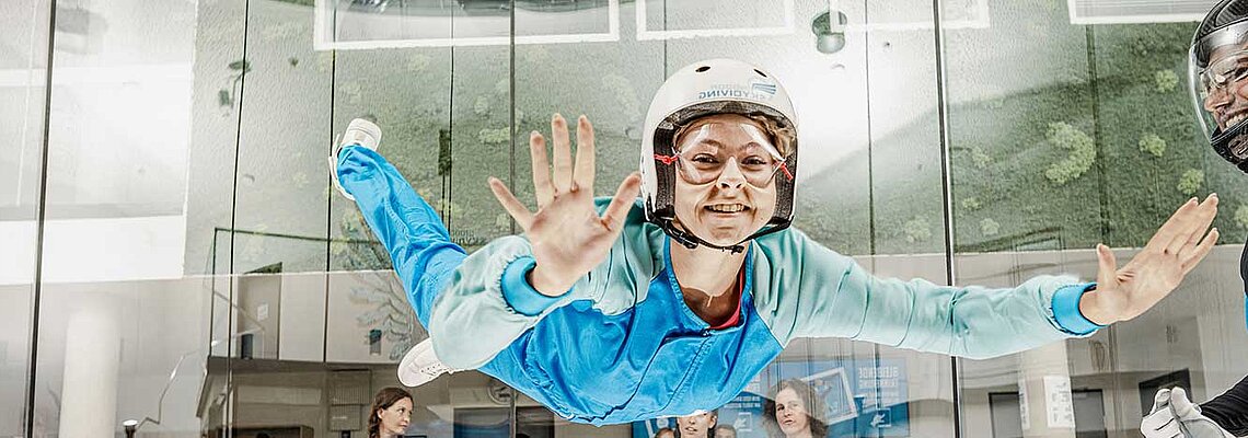 Auf dem Bild ist eine Frau in einem blauen Anzug beim Skydiving zu sehen.