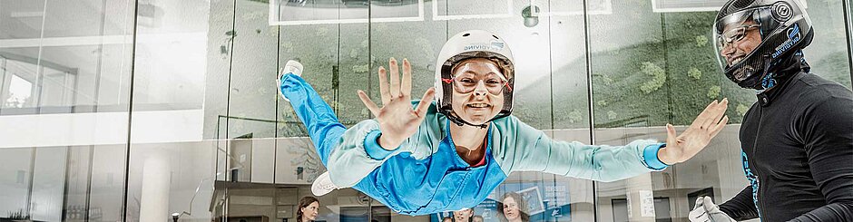 Auf dem Bild ist eine Frau in einem blauen Anzug beim Skydiving zu sehen.