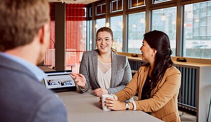 Ein Mann und zwei Frauen unterhalten sich in einem Büroraum
