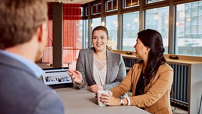 Ein Mann und zwei Frauen unterhalten sich in einem Büroraum