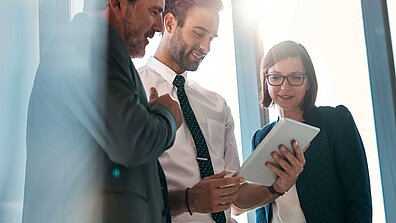 Two men and a woman in business attire looking at a brochure