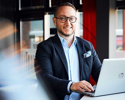 Auf dem Bild ist ein junger Mann im Anzug zu sehen, der an seinem Laptop sitzt. Es handelt sich um unseren Leasing-Experten Szymon Skwierczyynski.