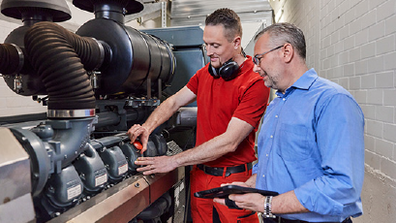 One man is working on a pipe, another is looking over his shoulder.