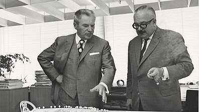 Black and white photograph with Werner Otto and another person standing in front of a building plan