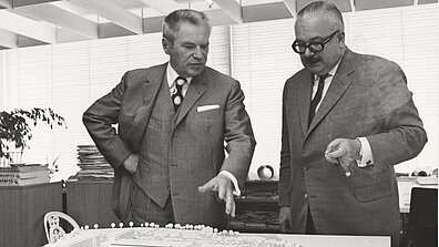 Black and white photograph with Werner Otto and another person standing in front of a building plan