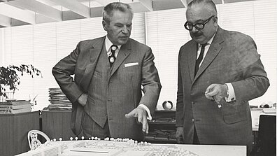 Black and white photograph with Werner Otto and another person standing in front of a building plan
