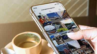 A person holds a mobile phone and looks at ECE&#039;s Instagram profile.