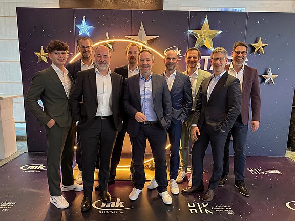 Eine Gruppe von mehreren Personen im Anzug steht vor der Kamera.