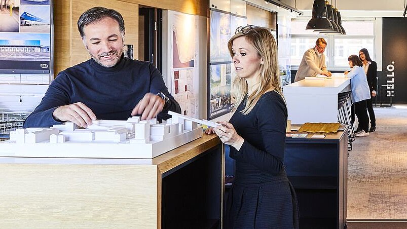 In the foreground and background, people stand in front of an architectural model