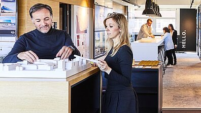 Im Vorder- sowie im Hintergrund stehen Personen vor einem Architekturmodell