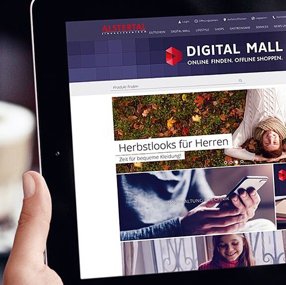 Eine Person hält ein Tablet, auf dem die Startseite "Digital Mall" angezeigt wird.