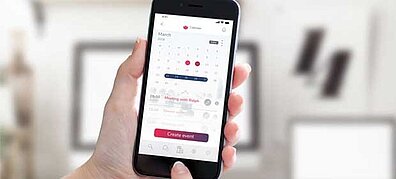 A person holds a smartphone with a calendar displayed on the screen