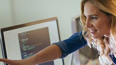 Sarışın bir kadın ekrandaki bir şeyi başka bir kişiye gösterir.