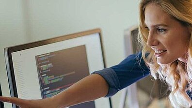 A blonde woman shows something on a screen to another person.