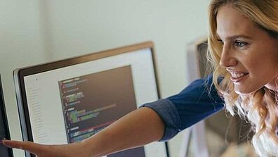 Eine blonde Frau zeigt einer anderen Person etwas auf einem Bildschirm.