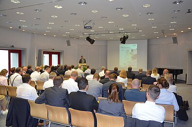 People in respectable work clothes listen to a presentation on a screen