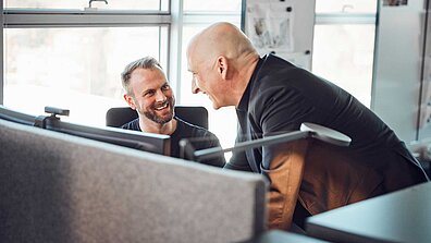 Es sind zwei Männer zu sehen, die an einem PC stehen.