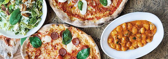 A laid table with two pizzas, a salad and gnocchi can be seen.