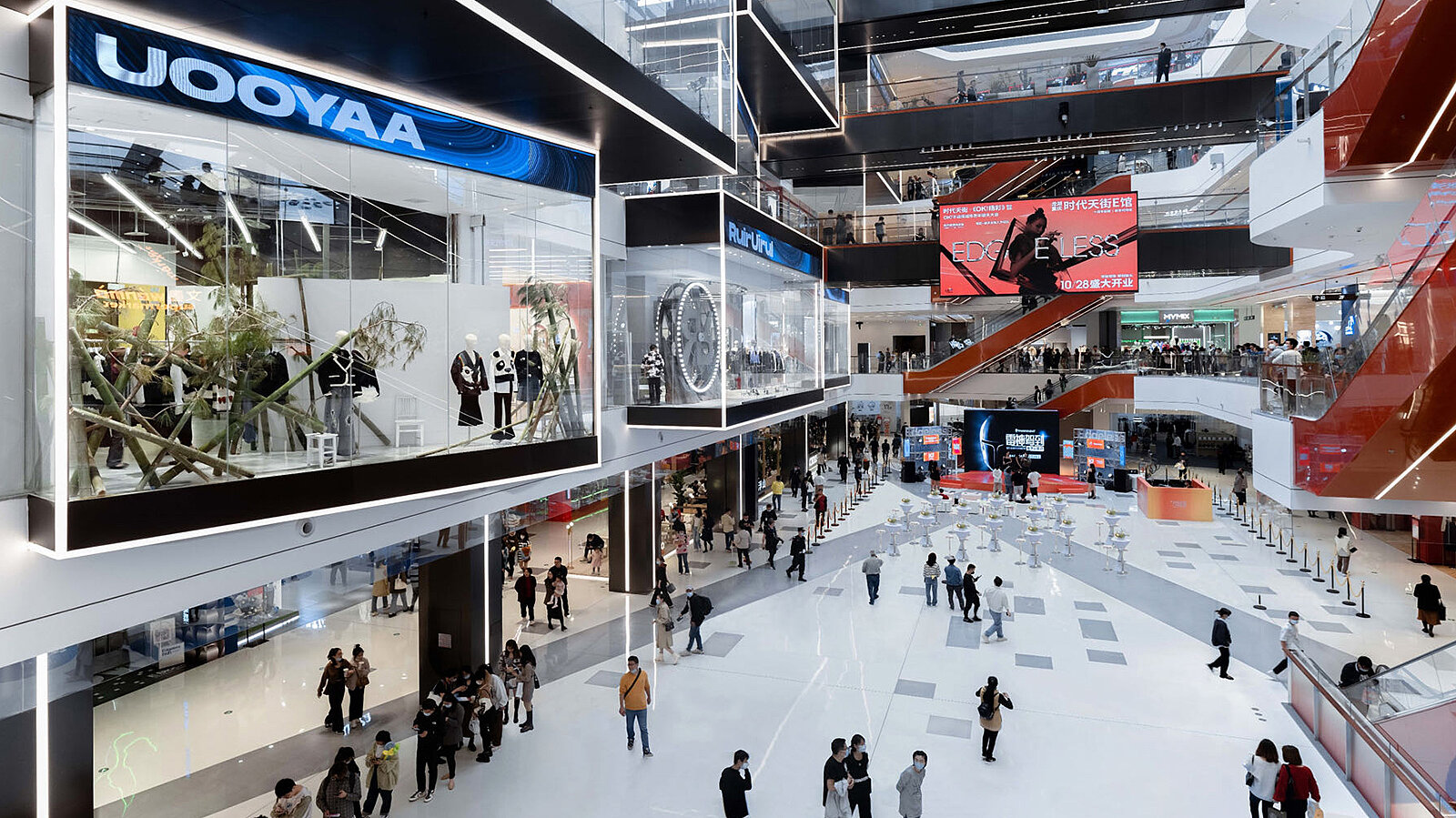 Blick in ein modern gestaltetes Einkaufszentrum mit außergewöhnlich gebauten Schaufenstern und vielen Menschen.