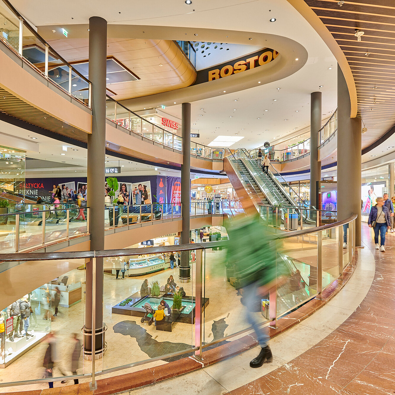 Das Innere der Galeria Bałtycka in Danzig mit mehreren Etagen, Rolltreppen und Geschäften. Es ist ein heller, offen gestalteter Flur im Inneren des Einkaufzentrums.