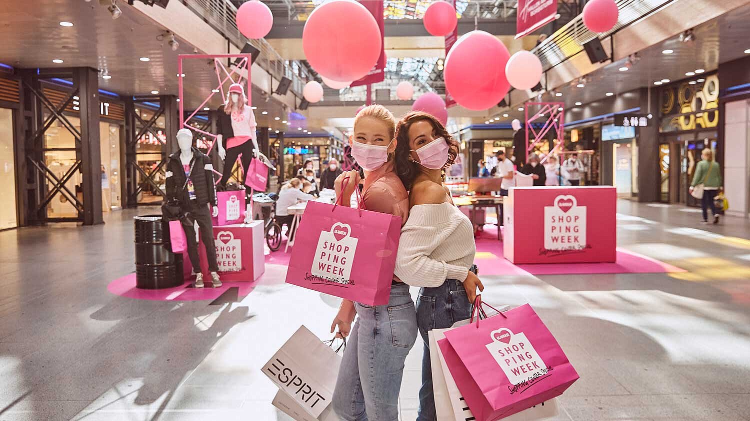 Two women walk through a mall decorated in pink with shopping bags