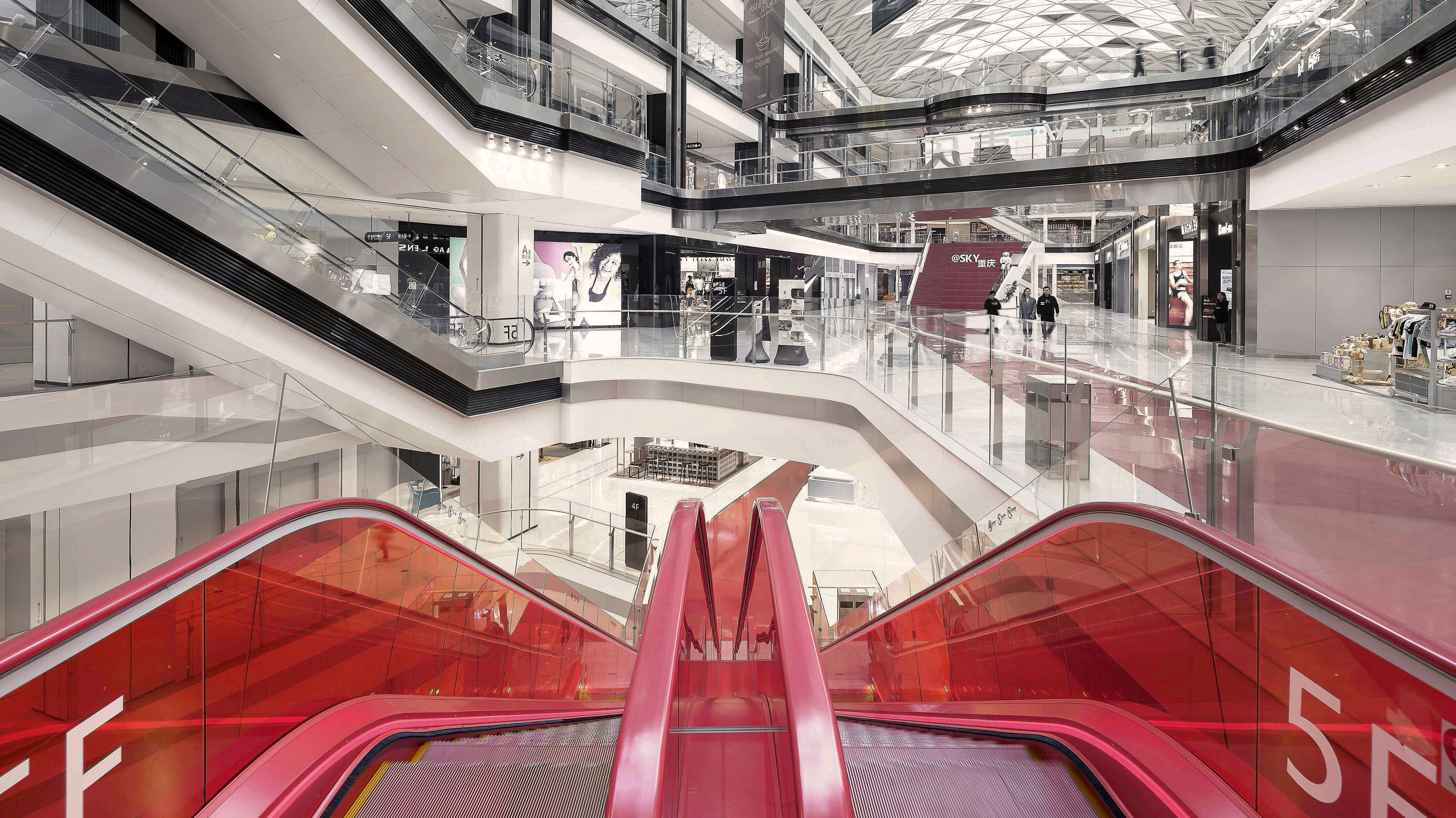 Innenansicht eines Einkaufszentrums mit auffälliger roter Rolltreppe und einem modern weiß gestalteten Innenbau.