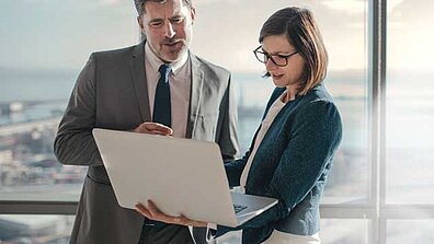 Two people in formal dress looking at a laptop together