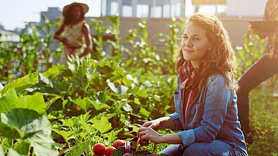 A woman kneels by the vegetable patch with a basket full of fresh vegetables.