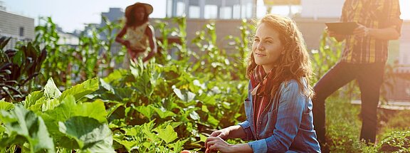 A woman kneels by the vegetable patch with a basket full of fresh vegetables.