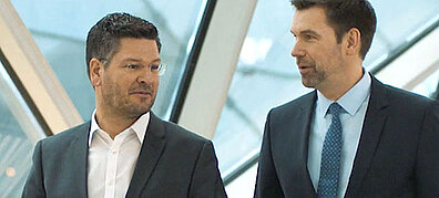 Two men in business attire stand next to each other