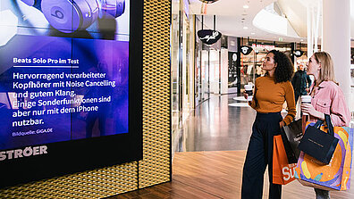 Zwei Damen mit Shopping-Tüten begutachten einen Flachbildschirm in einem Shopping-Center