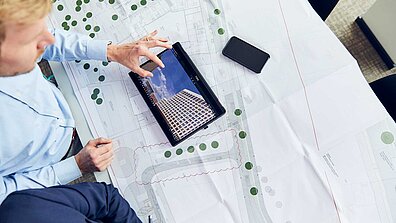 A person sits in front of a project plan and works on a tablet