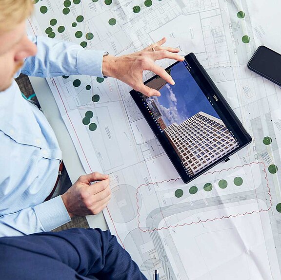 Eine Person sitzt vor einem Projektplan und arbeitet an einem Tablet