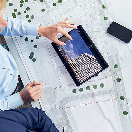 Eine Person sitzt vor einem Projektplan und arbeitet an einem Tablet