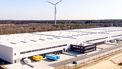 Aerial view of a huge white logistics building with parked lorries.