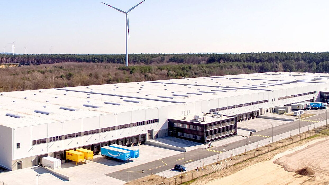 Aerial view of a huge white logistics building with parked lorries.