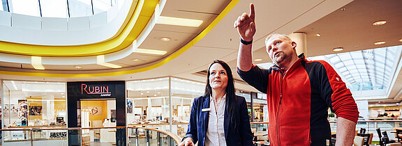 Es sind eine Frau und ein Mann im Center abgebildet, die über etwas diskutieren.